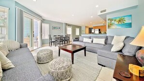 A living room with a grey sofa, two ottomans, a coffee table, and a painting of a beach scene. - Beachside Getaway with Patio and Parking (Newport Beach)