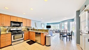 A modern kitchen with wooden cabinets, stainless steel appliances, and a dining area with a table and chairs. - Beachside Getaway with Patio and Parking (Newport Beach)
