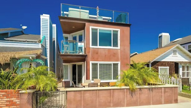 A two-story house with a balcony, a small porch, and a brick wall with plants. - Beachside Getaway with Patio and Parking (Newport Beach)