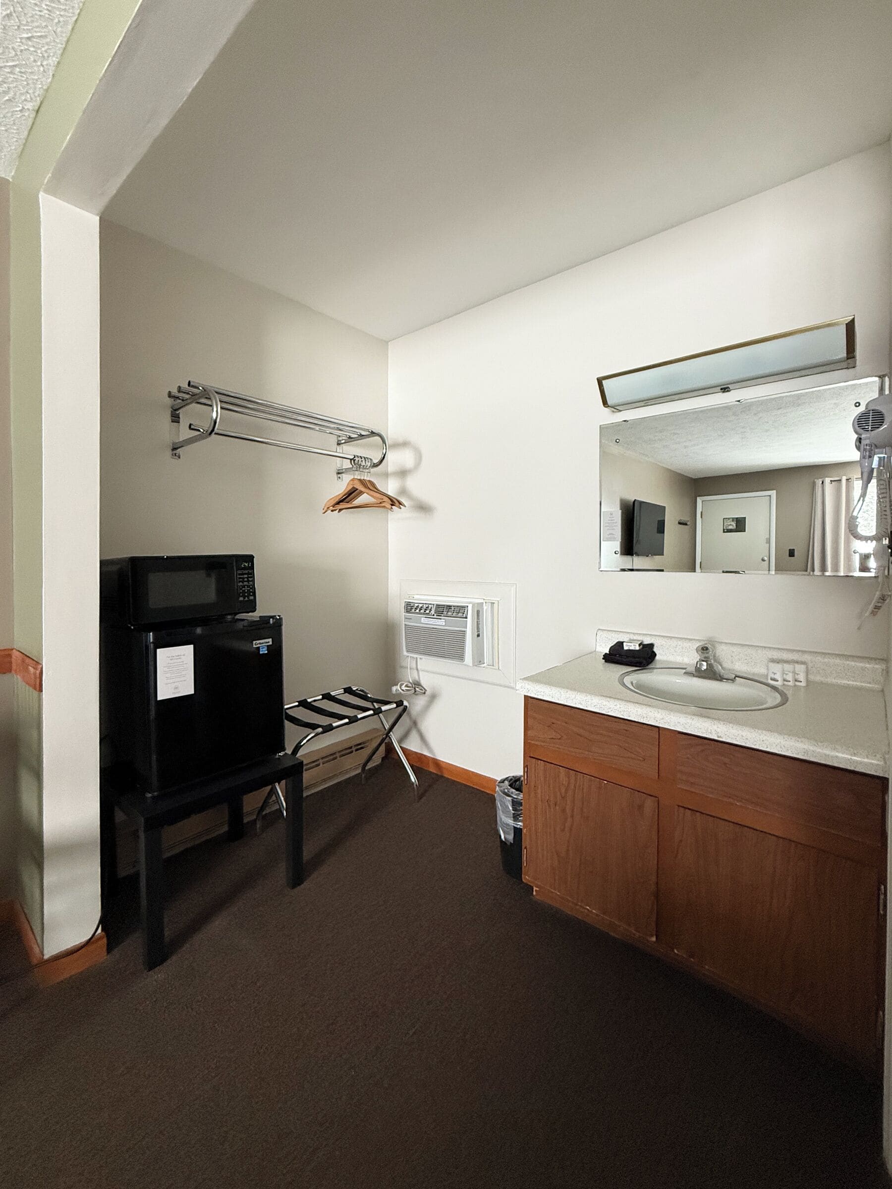 A compact hotel room with a kitchenette, a microwave, a small refrigerator, a sink, and a mirror.