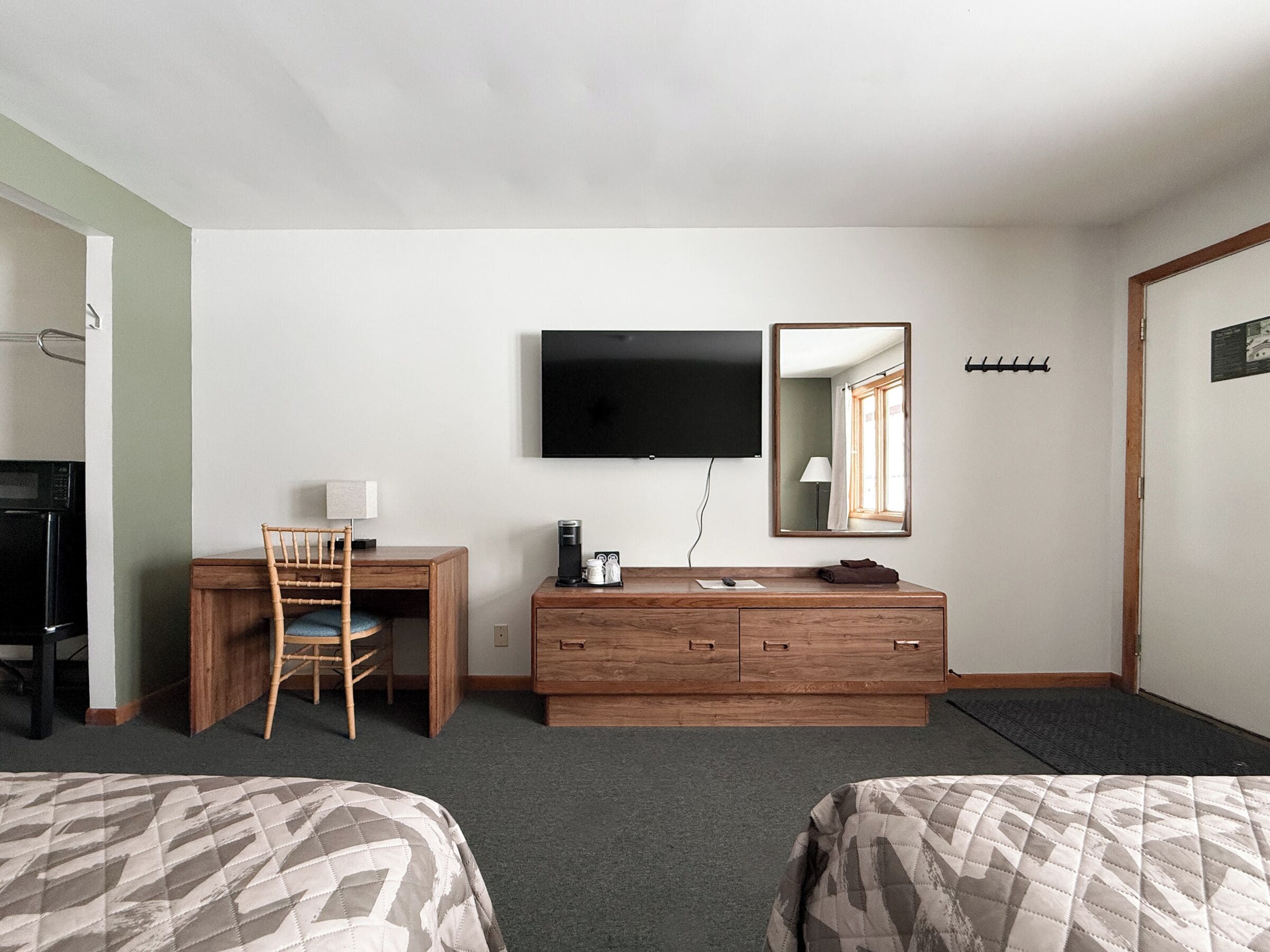 A hotel room with two beds, a desk with a chair, a television, a mirror, and a coffee maker.