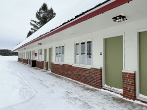 A row of motel rooms with brick lower levels and white upper levels, numbered 108, with a snow-covered ground. - The Trail Inn - Newberry, MI - 13467 M-28 (Newberry)