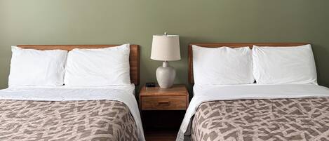 A hotel room with two beds, each with a wooden headboard, white bedding, and a patterned quilt. There is a nightstand with a lamp between the beds, and a star decoration on the wall.