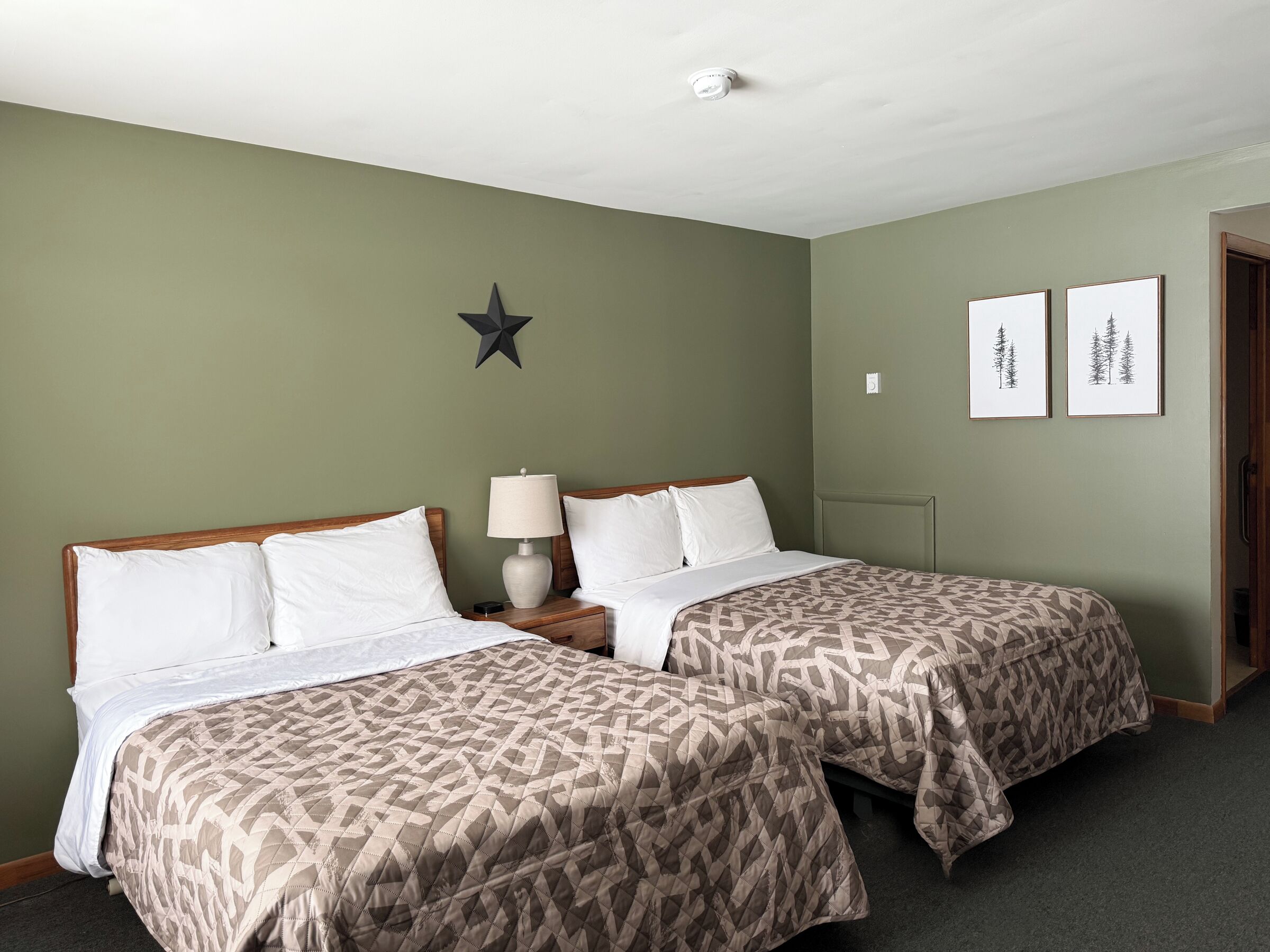 Una habitación de hotel con dos camas, una decoración con forma de estrella en la pared y dos cuadros enmarcados con paisajes de árboles.