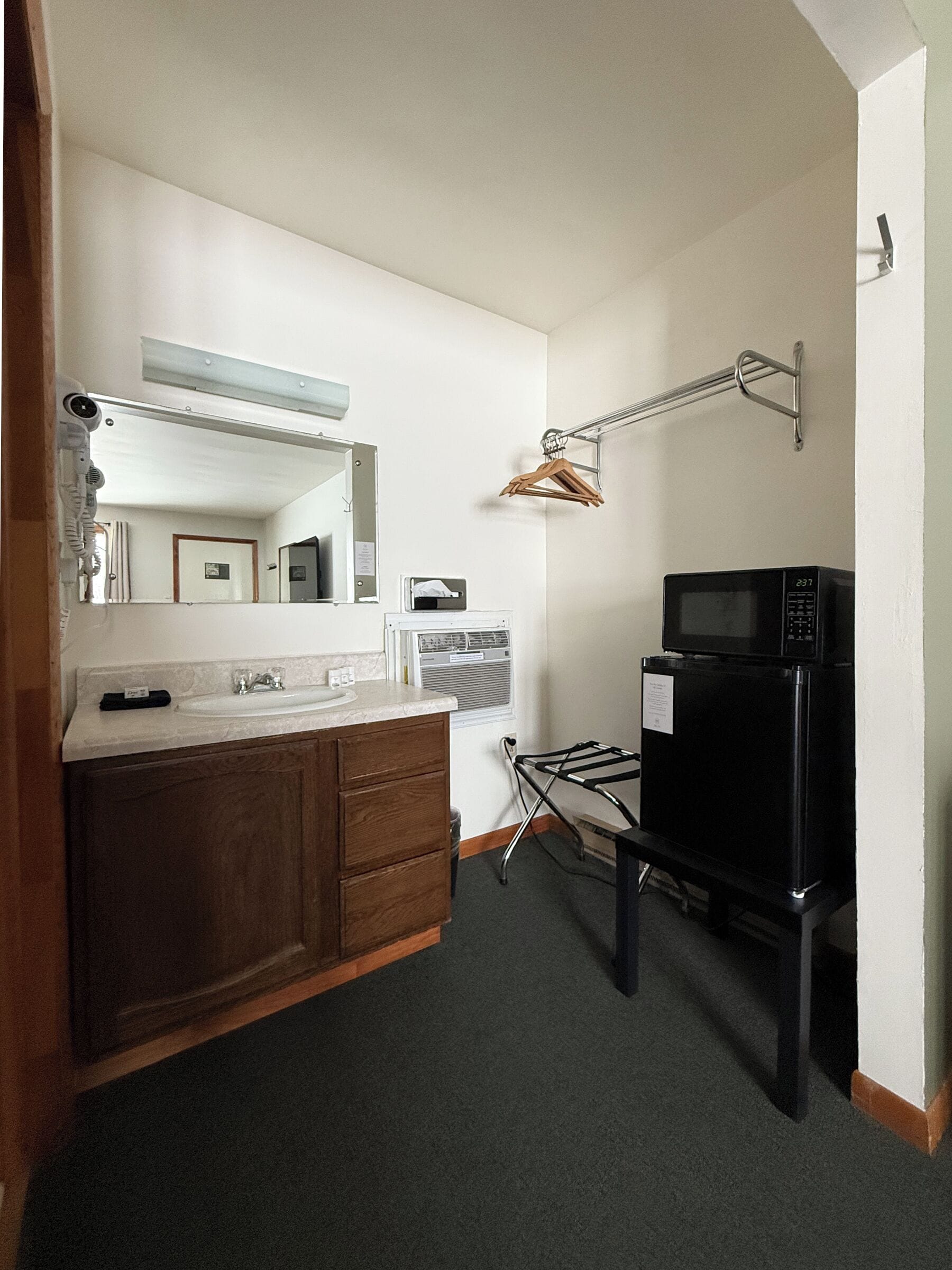 A compact kitchen with a sink, wooden cabinets, a microwave, and a clothes drying rack.