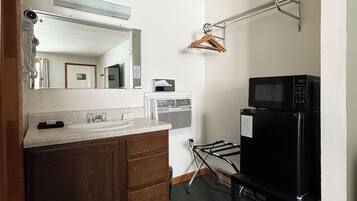 A compact kitchen with a sink, wooden cabinets, a microwave, and a clothes drying rack.
