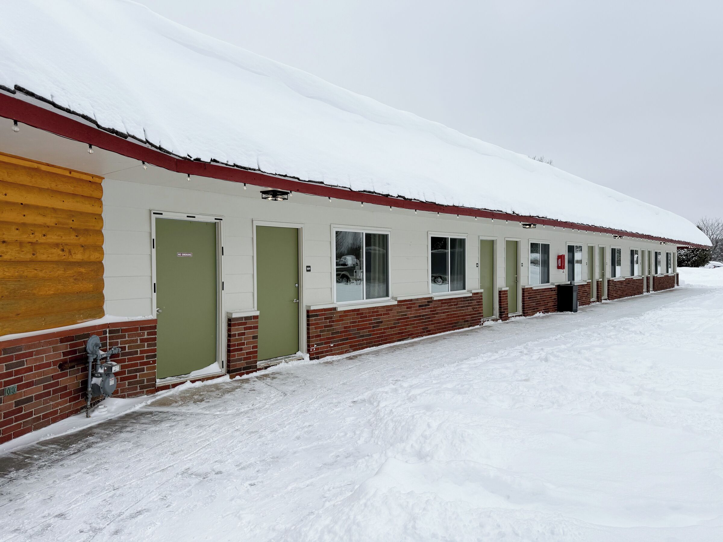 Rivissä motellihuoneita, joiden ulkoseinät ovat tehty tiilestä ja puusta. Jokaisessa huoneessa on ovi ja ikkuna, ja kaikki ovat lumen peitossa.