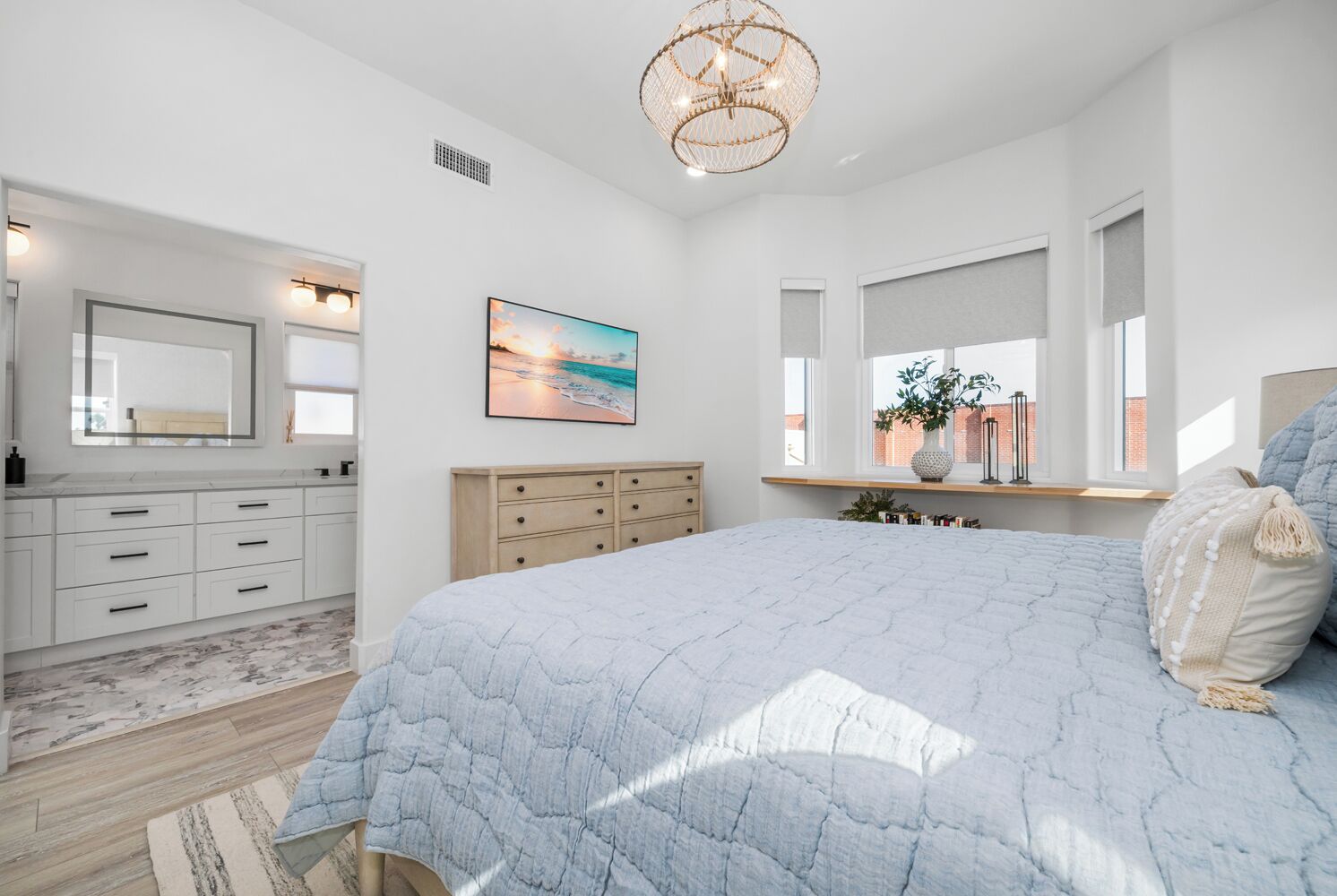 A bedroom with a large bed, a dresser, a vanity with a mirror, and a window with a view of a brick building.