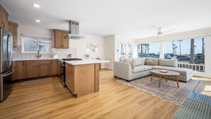 Une cuisine moderne avec des meubles en bois, un îlot central et une grande fenêtre donnant sur un parking.