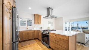 Une cuisine moderne avec des meubles en bois, un réfrigérateur en acier inoxydable, une cuisinière à gaz et une grande fenêtre donnant sur un parking.