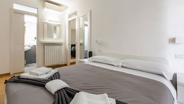 Una habitación de hotel moderna con una cama grande, un vestidor, un espejo y un radiador.