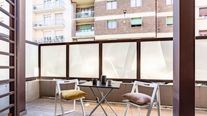 Un balcón con mesa y sillas, vista a un edificio de ladrillo y barandilla de metal.