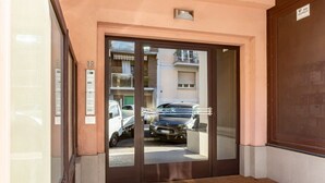 Una entrada de edificio con un escaparate de vidrio, una puerta marrón y un pequeño escalón que lleva hacia ella.