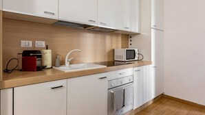 Una cocina moderna con armarios blancos, encimera de madera, un lavabo, un microondas y un electrodoméstico rojo.
