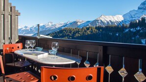 A table with a mountain view, orange chairs, and wine glasses.