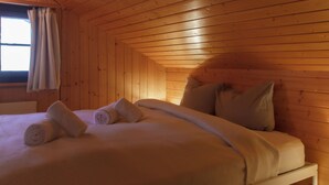 A wooden cabin room with a bed, pillows, and a window with curtains.