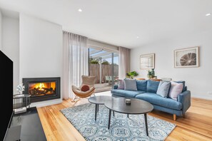 Ein modernes Wohnzimmer mit Kamin, einem blauen Sofa, einem Couchtisch und Blick ins Freie.
