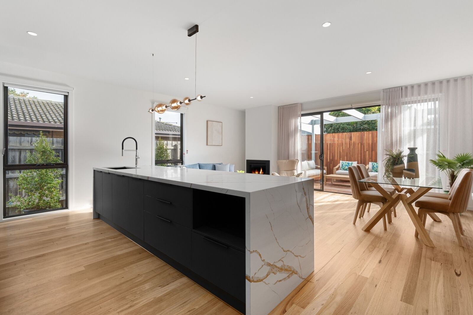 A modern kitchen with a marble island, black cabinets, and a dining area with wooden chairs and a glass table.