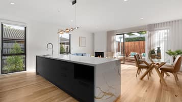 A modern kitchen with a marble island, black cabinets, and a dining area with wooden chairs and a glass table.