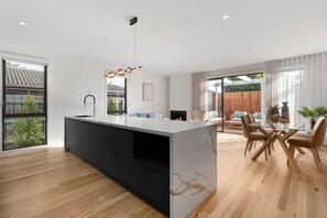 A modern kitchen with a marble island, black cabinets, and a dining area with wooden chairs and a glass table. - Rye Local #3- Luxe townhouse, 300m to beach Linens incl -live like a local! (Rye)
