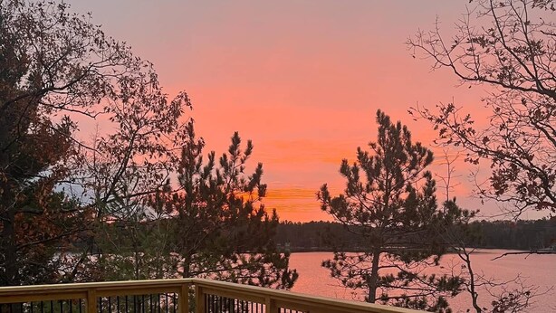Une terrasse en bois avec deux fauteuils Adirondack donnant sur un lac au coucher du soleil.