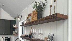 Une cuisine avec des plans de travail sombres, un lambris blanc et des étagères murales en bois où sont disposés divers objets.