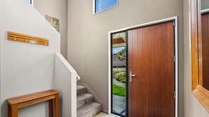 Un hall d’entrée moderne avec un banc en bois, une porte en verre et un escalier menant à un espace extérieur.