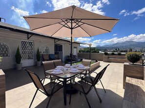 An outdoor patio with a table set for four, surrounded by chairs, under a large umbrella.