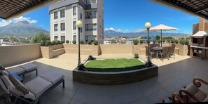 A rooftop terrace with a view of a mountain, outdoor seating, and a barbecue area.