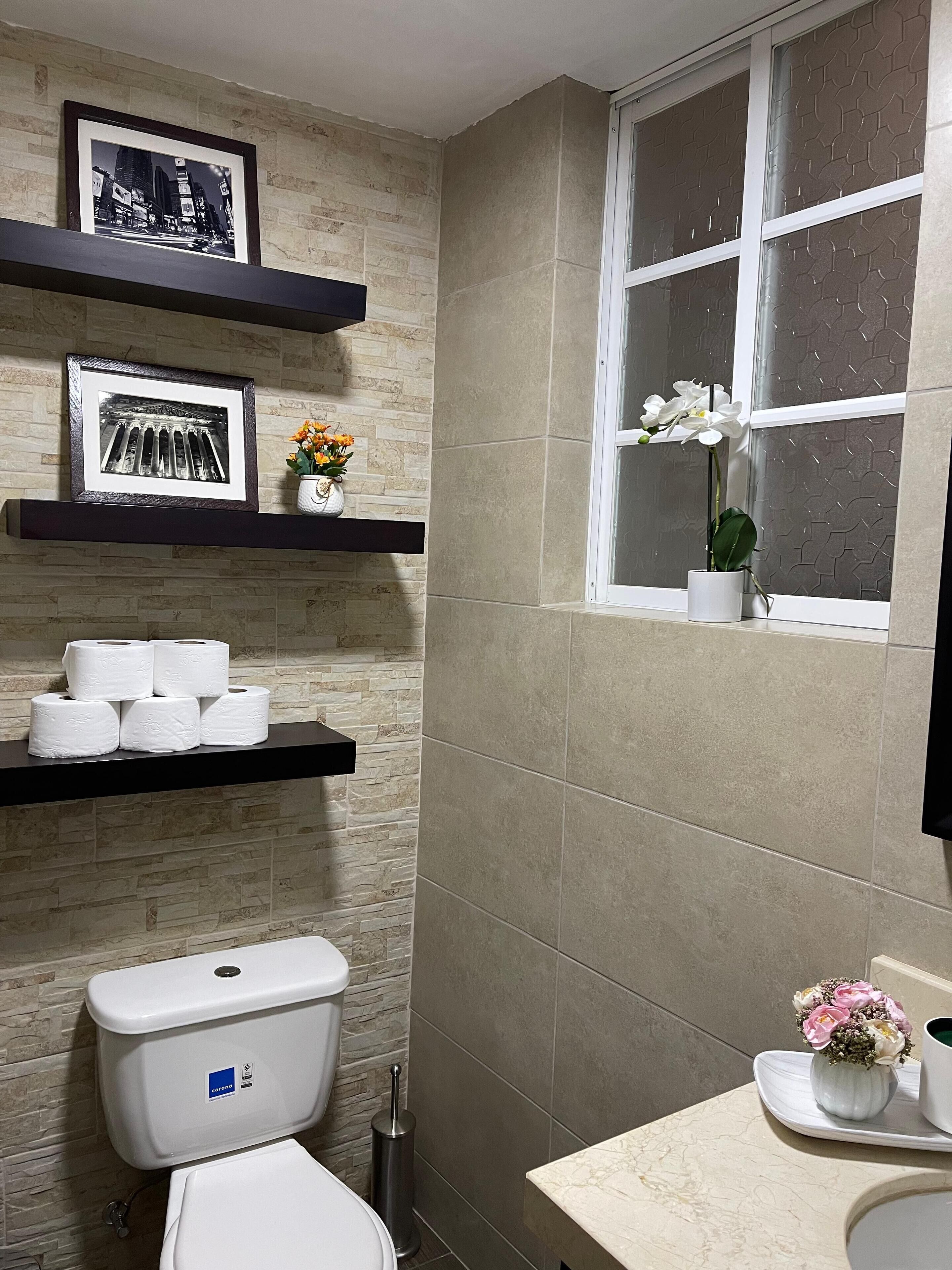 Un bagno con il water, un lavandino, una finestra vista e mensole con articoli da toilette e quadri incorniciati.