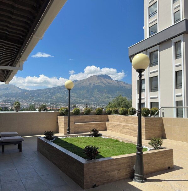 A rooftop terrace with a view of a mountain, a landscaped garden, and a modern building.
