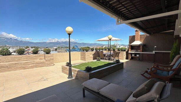A rooftop patio with a grill, seating area, and a view of mountains.