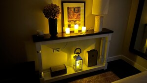 A console table with a framed picture, a vase of dried flowers, and three lit candles.