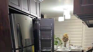 A kitchen with a stainless steel refrigerator, a built-in oven, and a metal rack shelf.