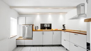 Eine moderne Küche mit weißen Schränken, einem Edelstahlkühlschrank, einer Kaffeemaschine und einer Holzausziehtafel.