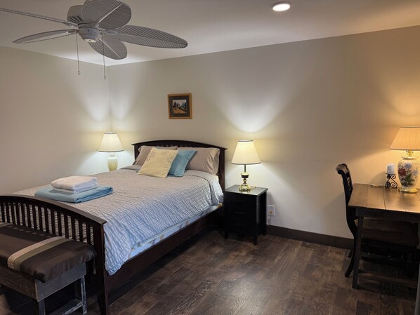 A neatly arranged bedroom with a bed, bedside tables, a chair, a desk, and a ceiling fan.