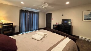 A hotel room with a bed, a desk, a television, and a ceiling fan. - Mara Spring Lodges - Suite 1 (Mara)