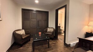 A compact living space with a dark wood floor, a glass-top coffee table, two leather sofas, and a dark wooden wardrobe. - Mara Spring Lodges - Suite 1 (Mara)