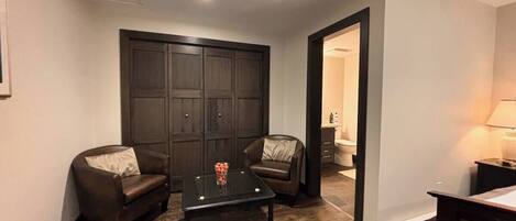 A compact living space with a dark wood floor, a glass-top coffee table, two leather sofas, and a dark wooden wardrobe.