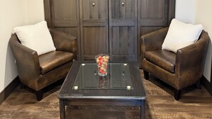 A room with two leather armchairs, a glass coffee table, and a large wooden wardrobe. - Mara Spring Lodges - Suite 1 (Mara)