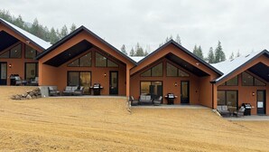 A modern building with large windows and a flat roof, situated on a sloped terrain with a gravel surface. - Mara Spring Lodges - Towhee Mountain Lodge 3 (Mara)