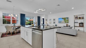 Uma cozinha moderna com uma ilha central, sala de jantar com cadeiras e uma sala de estar com sofá.