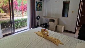 Een hotelkamer met een bed, een bureau, een televisietoestel en uitzicht op een tuin door de schuifdeur.