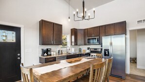A modern kitchen with dark wooden cabinets, stainless steel appliances, and a wooden dining table. - New Build w/ Hot Tub, Sauna, Arcade, Mountain Views (Florissant)