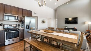 A modern kitchen with stainless steel appliances, a dining area with wooden furniture, and a living room with a flat-screen TV. - New Build w/ Hot Tub, Sauna, Arcade, Mountain Views (Florissant)