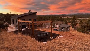 A modern house with a wooden deck and a small shed in a rural setting. - New Build w/ Hot Tub, Sauna, Arcade, Mountain Views (Florissant)