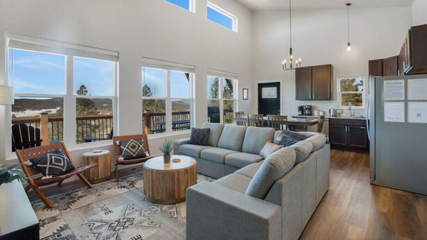 A spacious living room with a large sectional sofa, a wooden coffee table, and a view of a deck. - New Build w/ Hot Tub, Sauna, Arcade, Mountain Views (Florissant)