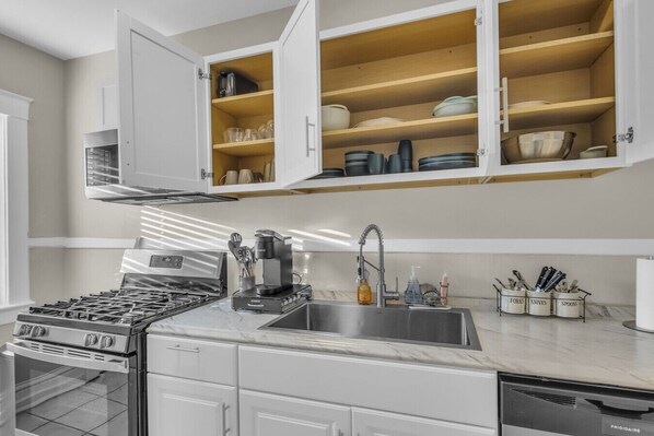 Una cocina moderna con armarios blancos, estufa integrada, cafetera y lavamanos.