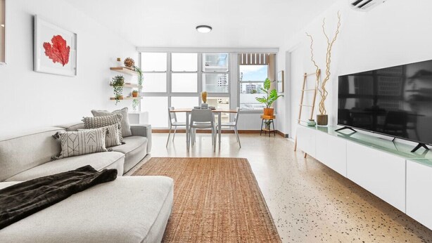 A modern living room with a sofa, a coffee table, a TV on a glass cabinet, and a dining area with chairs and a table.