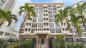 A multi-story hotel with a central entrance, surrounded by palm trees and a black fence.
